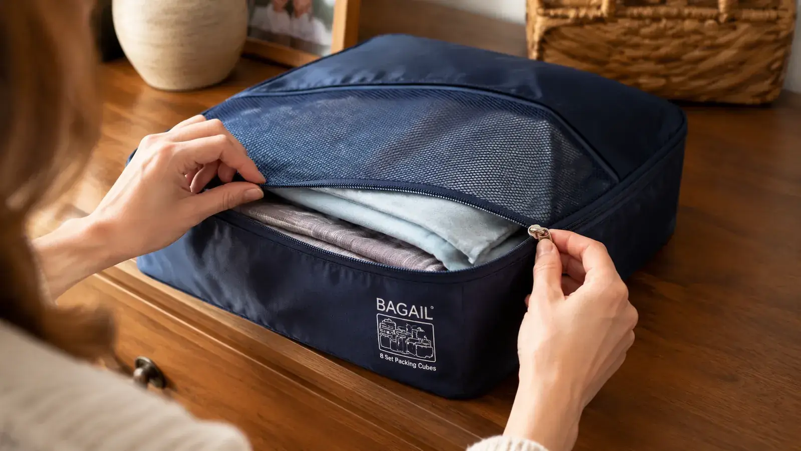 Hands unzipping a BAGAIL packing cube to reveal neatly folded shirts inside